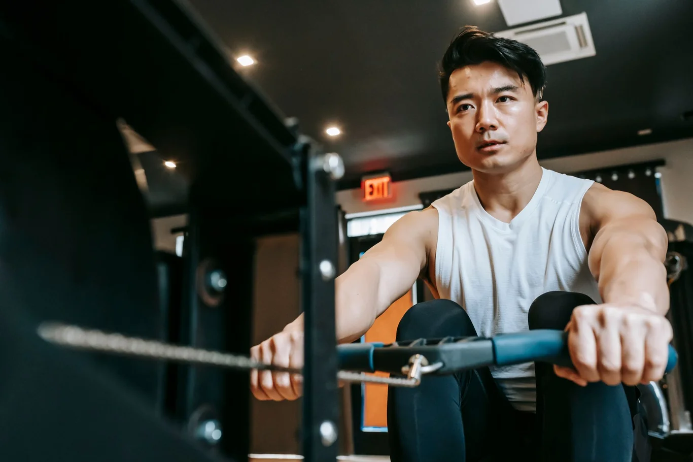 Man on a rowing machine mid-drive in a modern gym, gripping the handle with arms extended