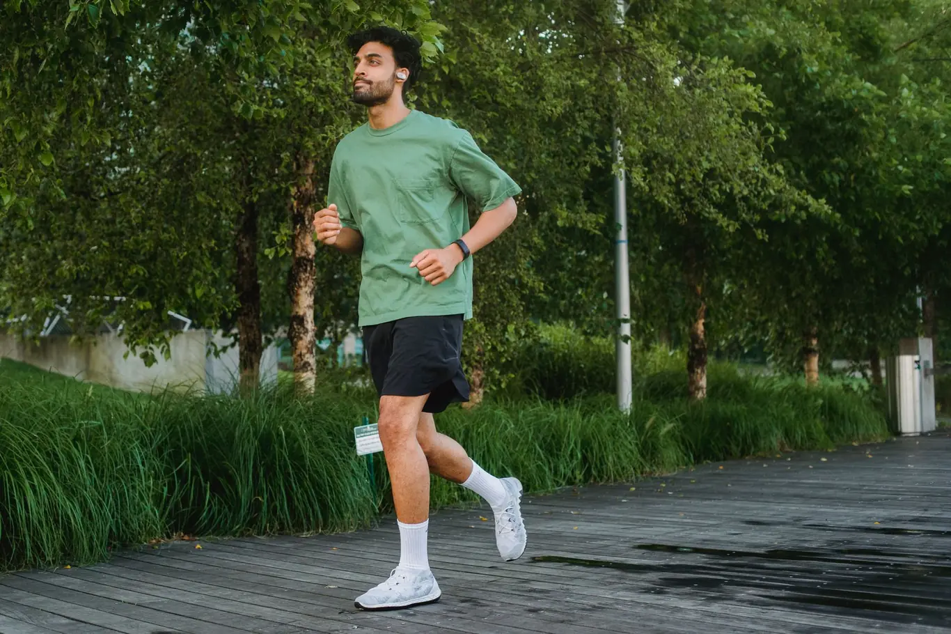 Man jogging outdoors on a park path wearing a smartwatch and running shoes