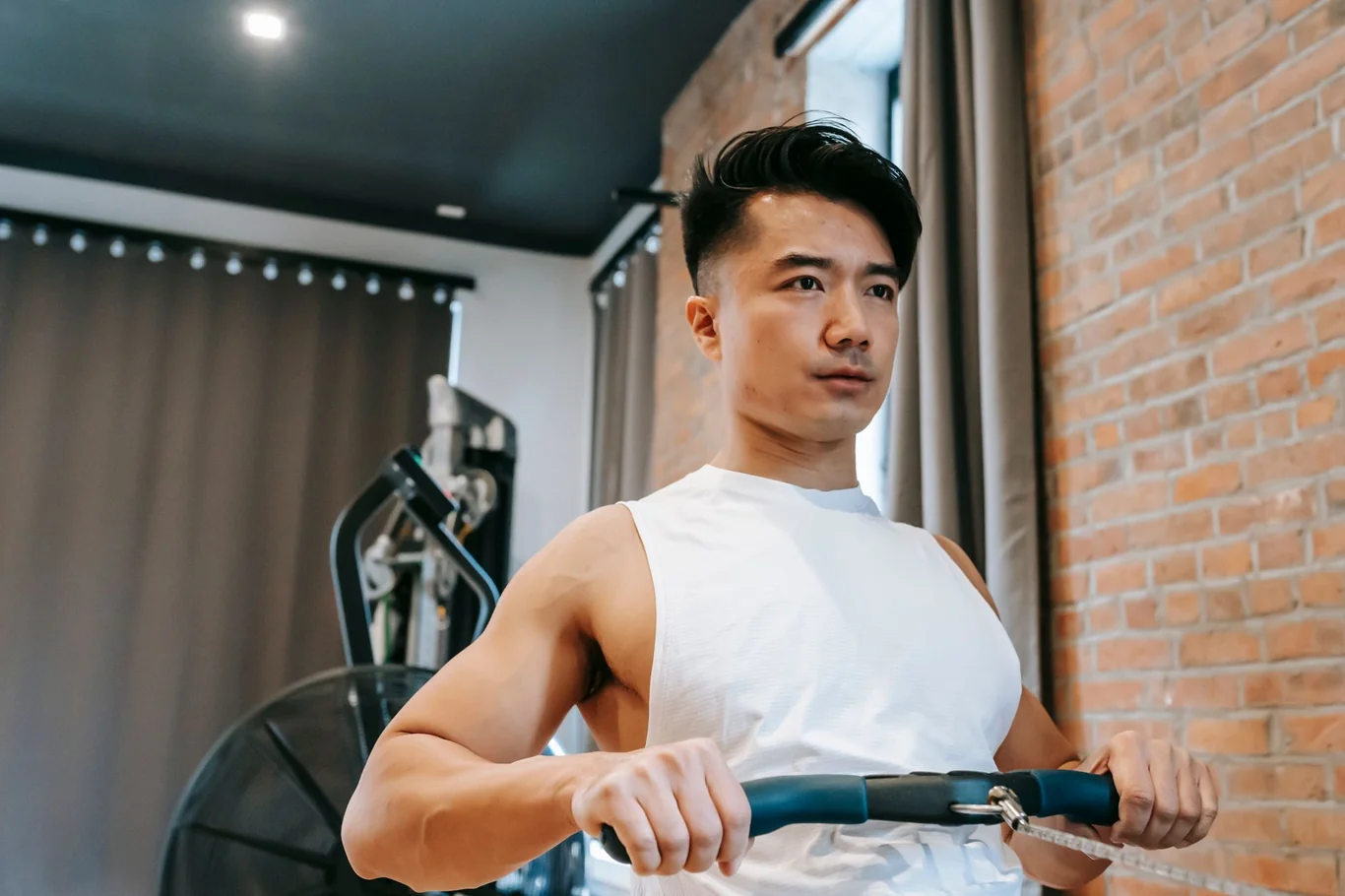 Man using a rowing machine in a home gym with brick walls and natural light