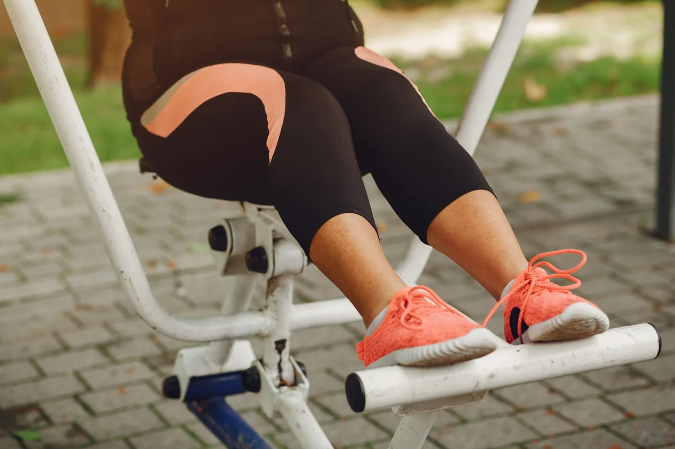 Close-up of a woman's legs stepping on an outdoor exercise stepping machine in coral sneakers