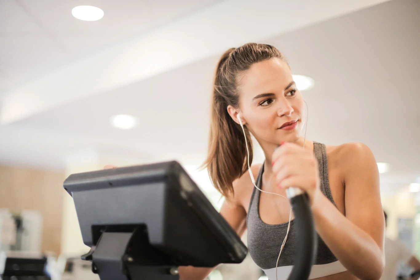 Woman pedaling a stationary bike at the gym with earbuds in