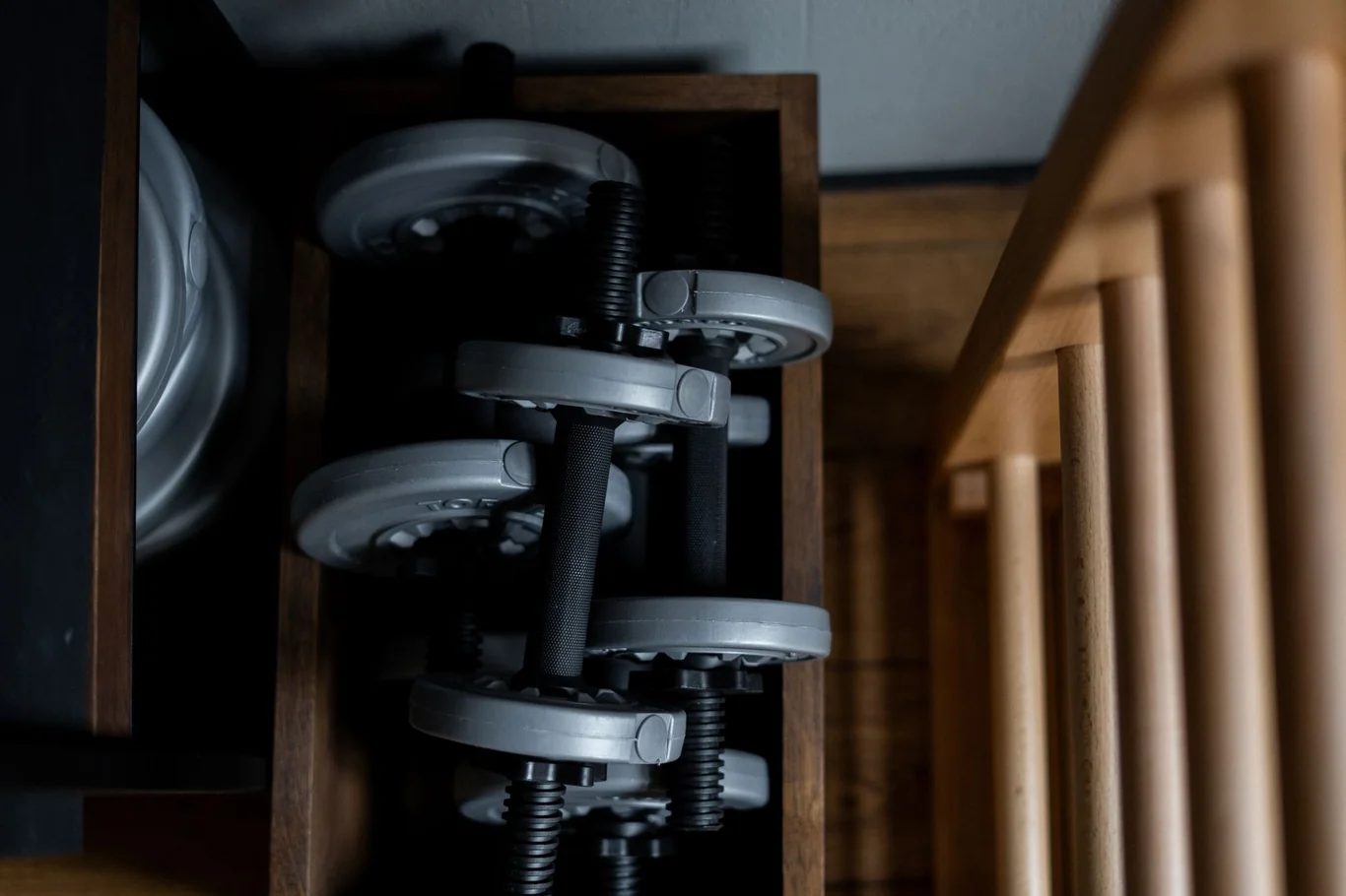 Adjustable dumbbells in a wooden storage rack in a home setting