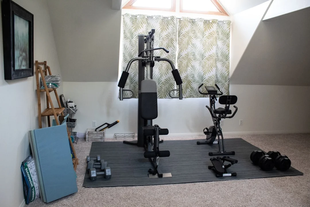 Wall-mounted cable pulley home gym machine beside a stationary bike on a mat