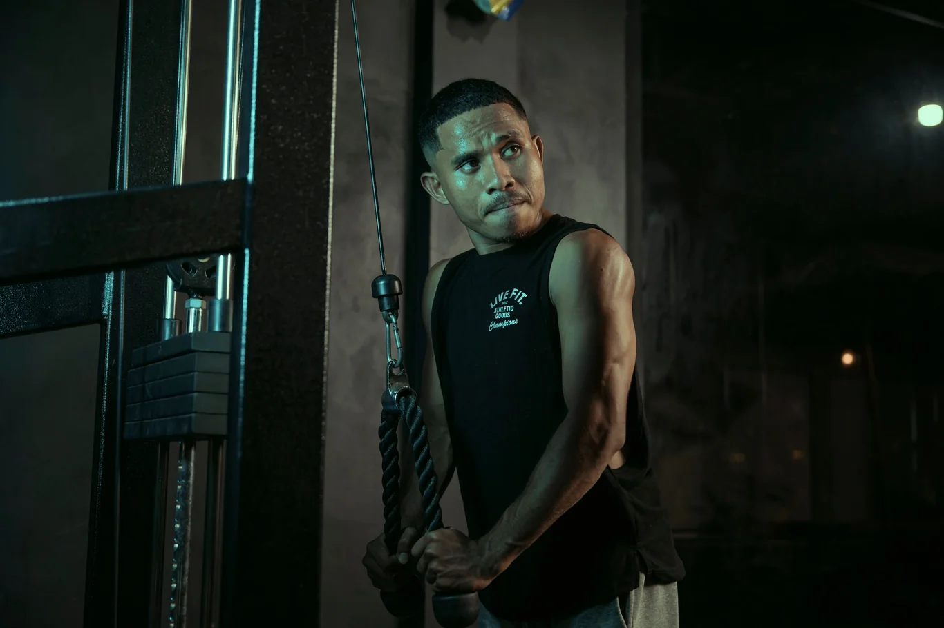 Man using a wall mounted cable pulley machine in a dimly lit gym