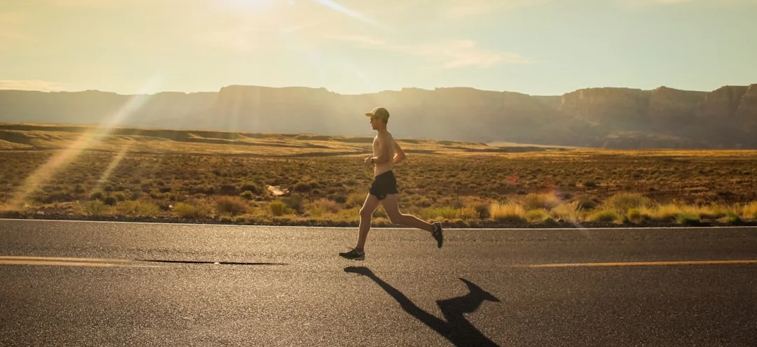 Lone runner on an open desert road at golden hour with red rock canyon in background