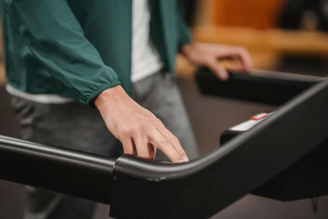 Person adjusting a treadmill with one hand resting on the side rail near the running belt