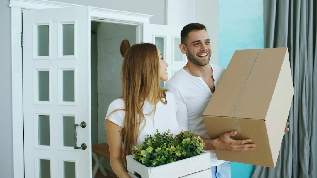 Couple carrying cardboard boxes through a home doorway