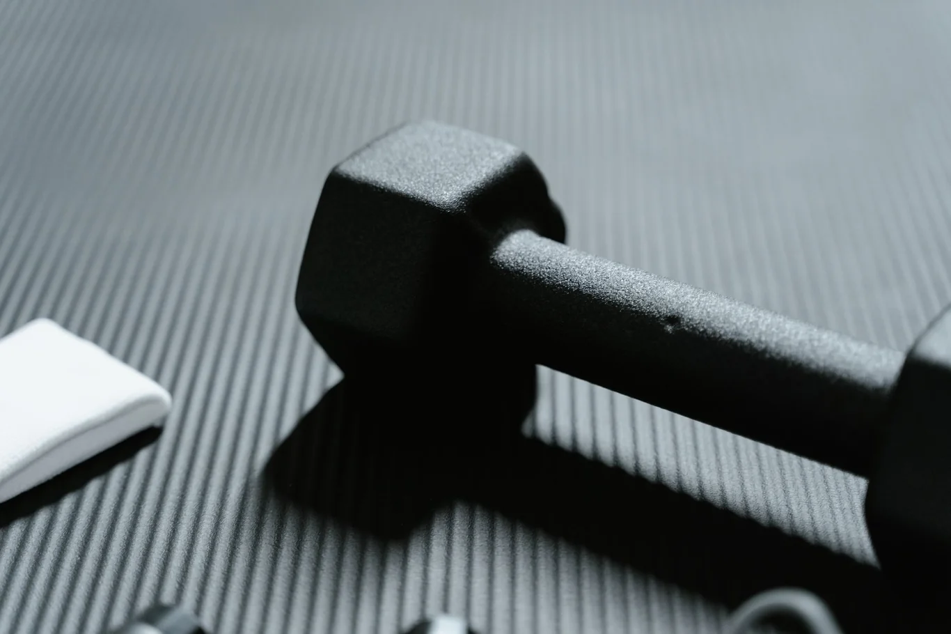 Black rubber exercise mat with a dumbbell resting on its textured ridged surface