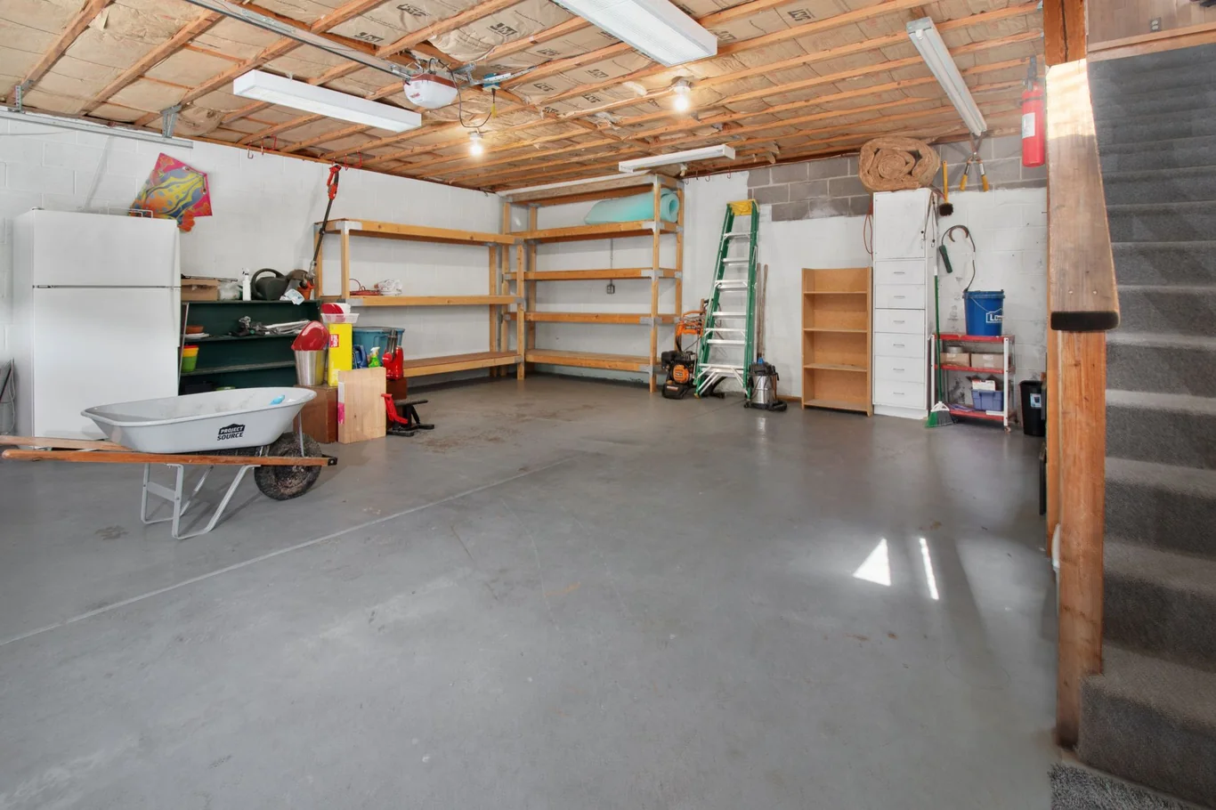 Spacious empty garage with concrete floor, wooden shelving, and overhead lighting ready for home gym equipment
