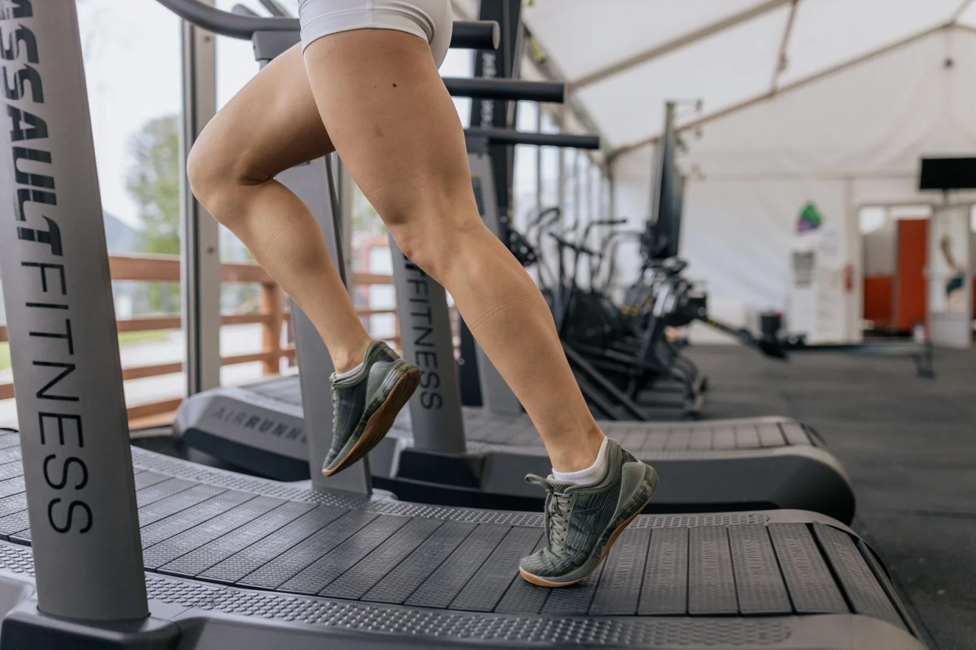Close-up of a runner on a commercial treadmill showing legs and sneakers on the running belt