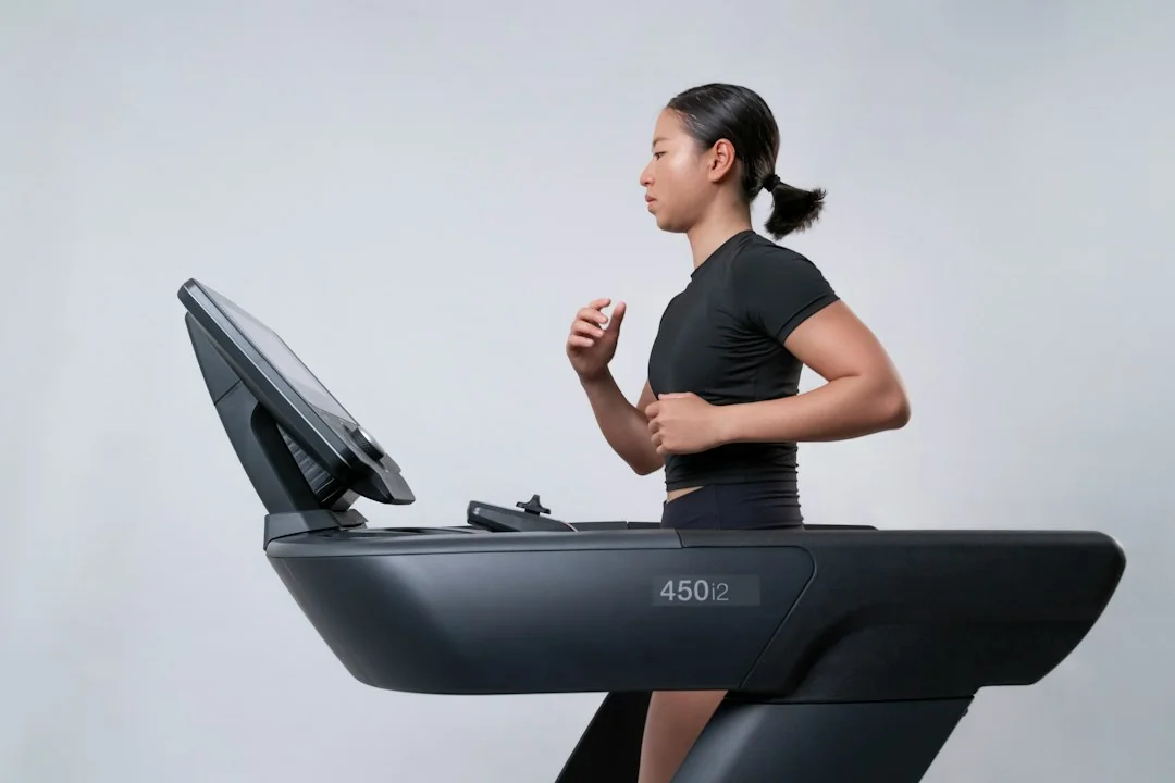 Woman in black workout clothes running on a dark treadmill with a large touchscreen console