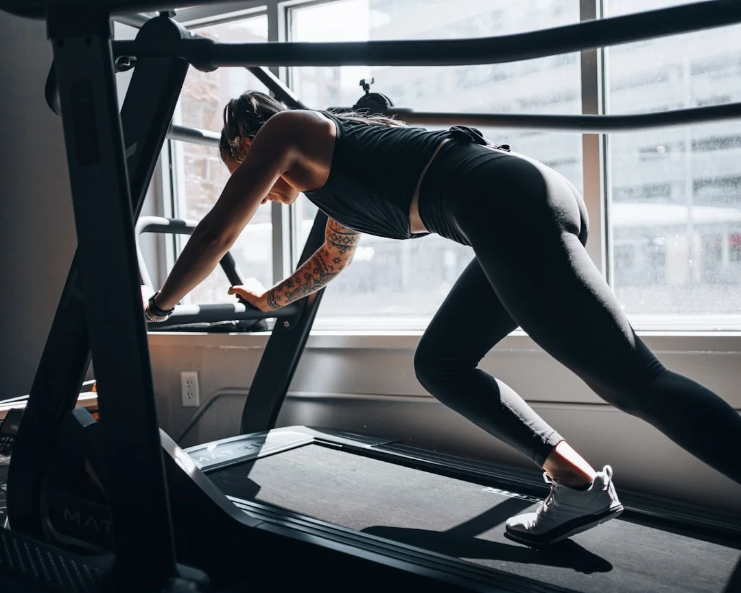 Woman in athletic wear leaning forward on a treadmill in a gym with large windows