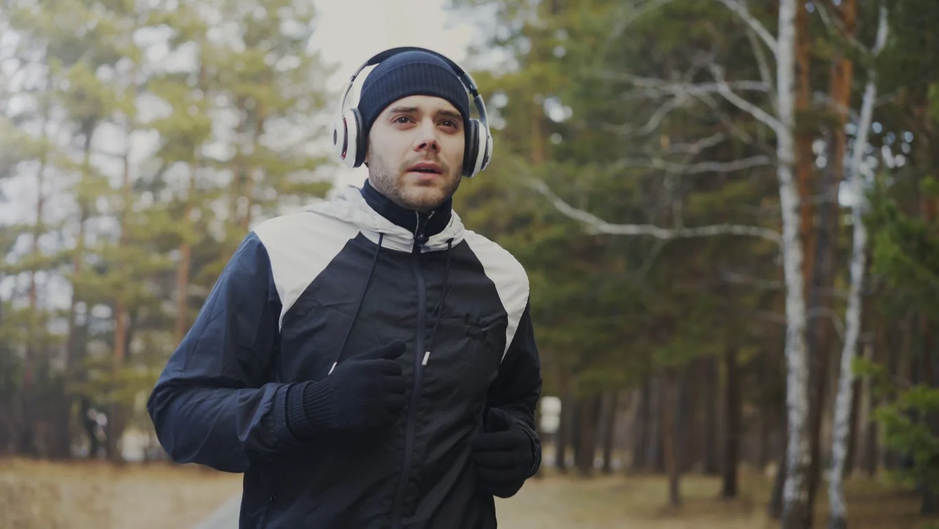 Man running outdoors in a park wearing large white headphones