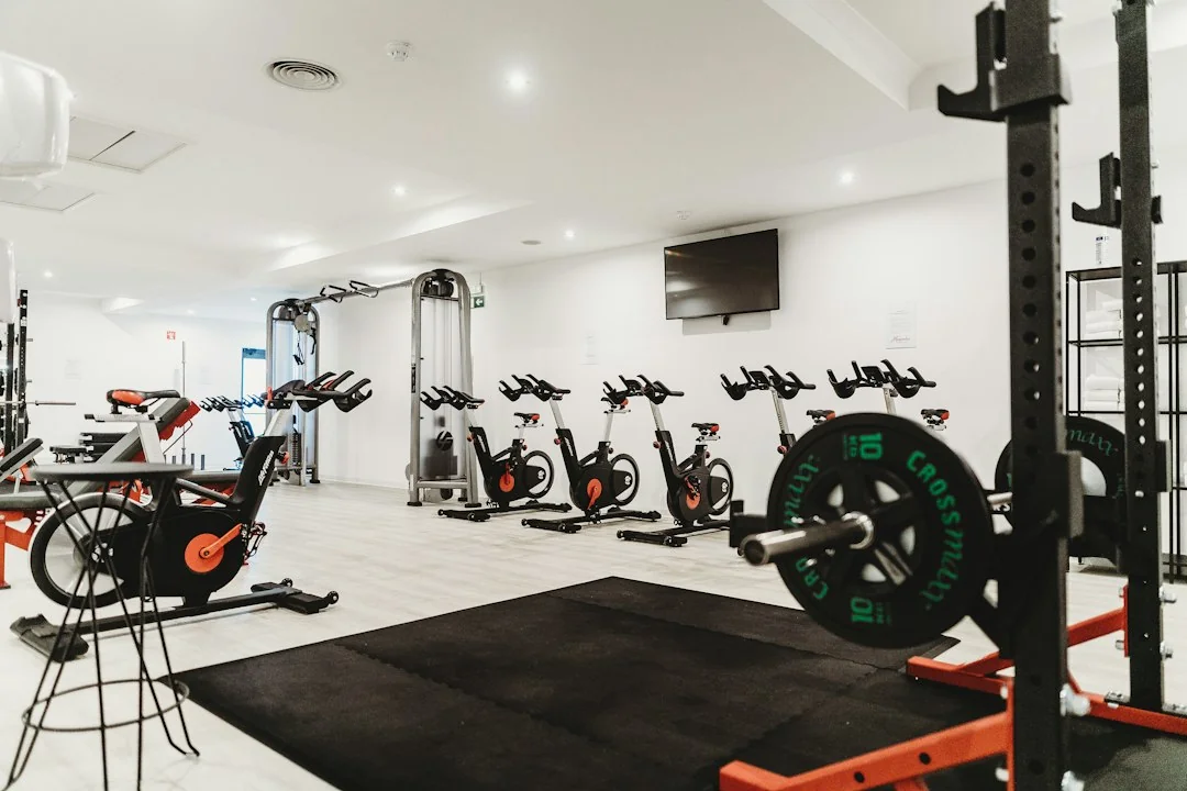 Row of indoor cycling bikes in a bright gym with weight equipment in the background