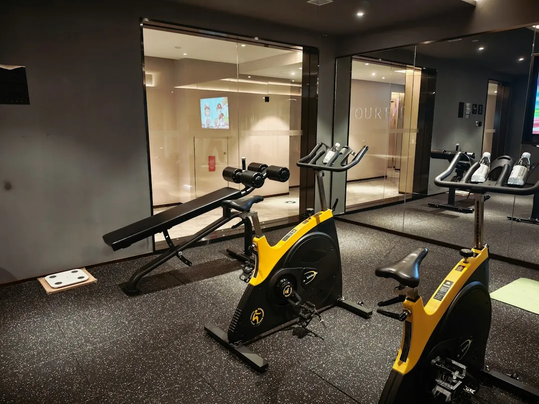Yellow spin bikes on a rubberized gym floor with treadmills visible through a glass partition