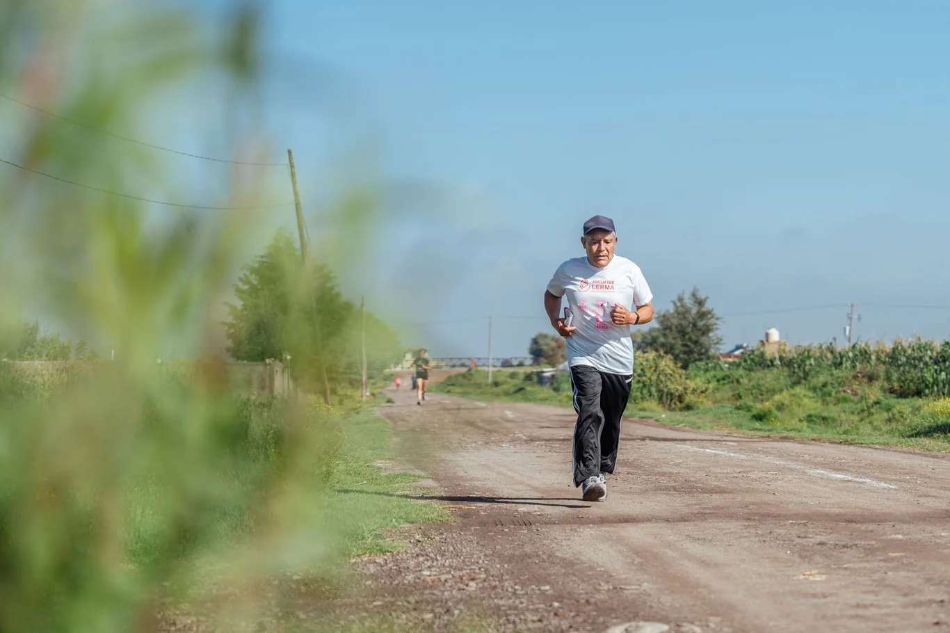 Older man jogging on a rural dirt road under a clear blue sky