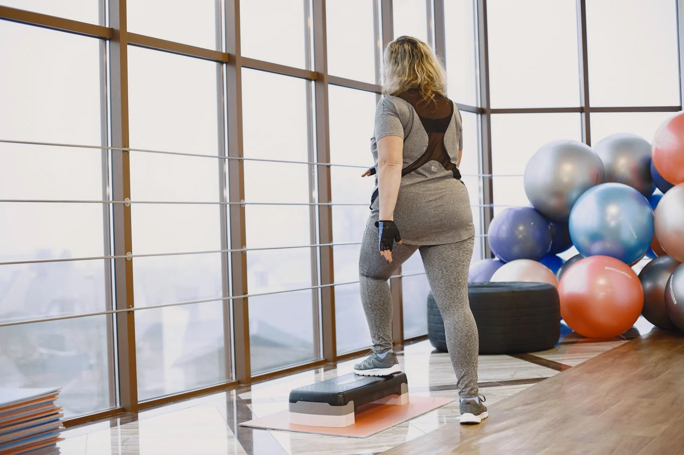 Woman exercising on an aerobic step platform in a bright gym with fitness balls in background