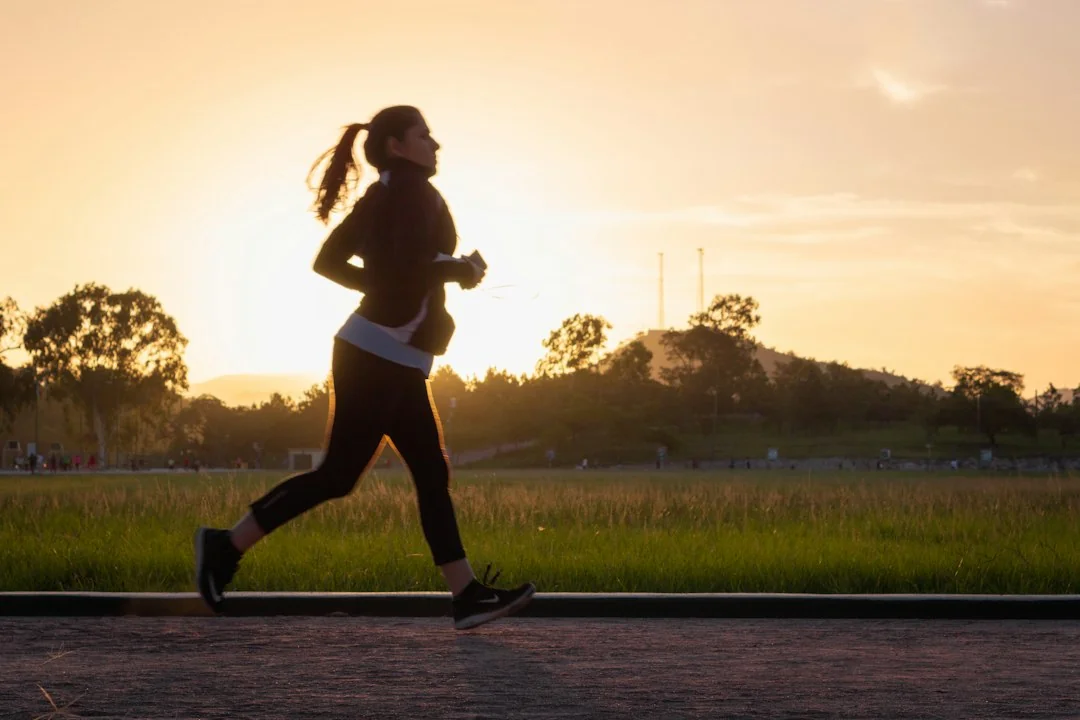 Woman jogging on a paved path at sunset with open fields behind her