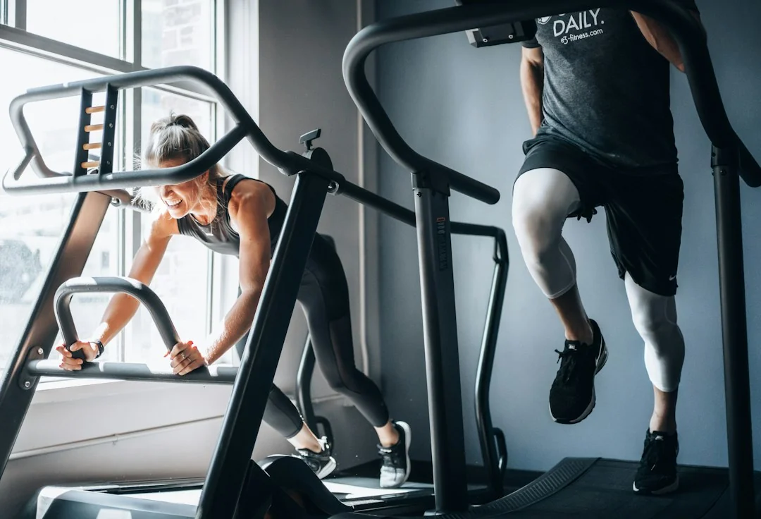 Two people working out on treadmills at a steep incline in a gym setting