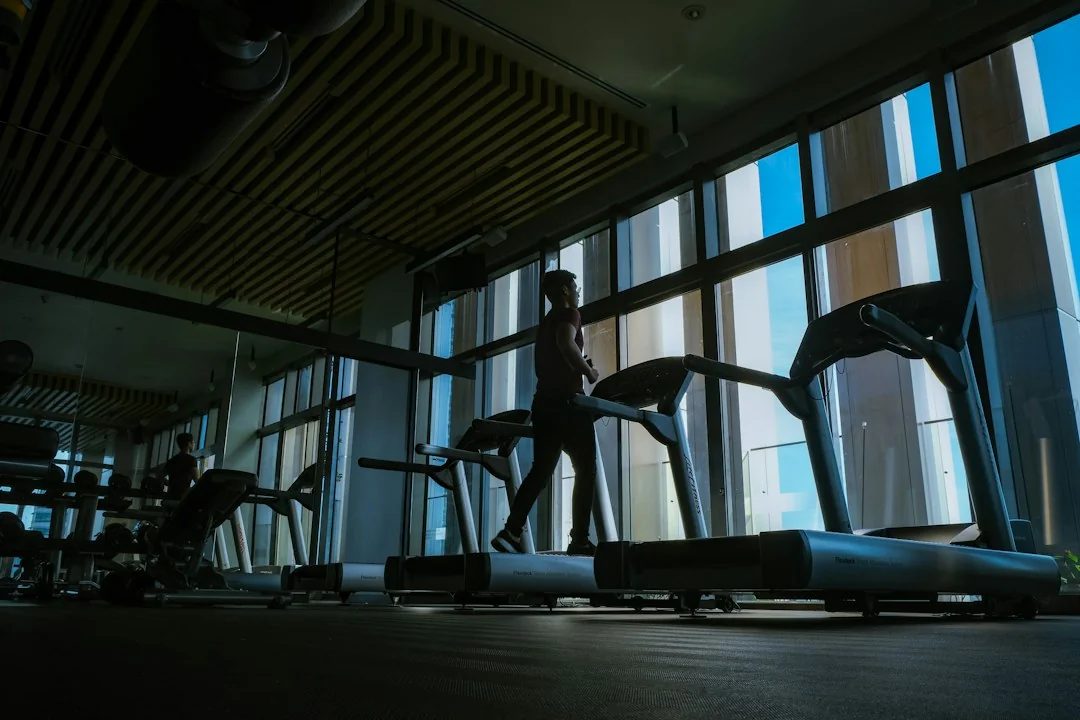 Person walking on a treadmill in a modern gym with floor-to-ceiling windows