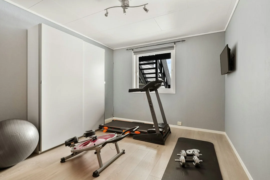 Home gym with a treadmill, rowing machine, and free weights in a bright spare room