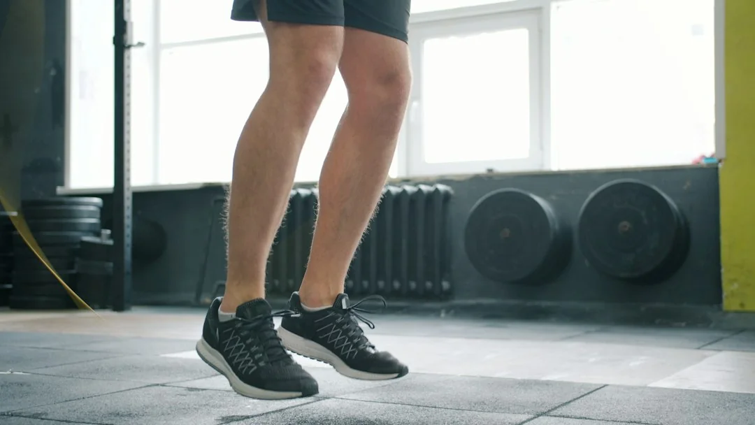 Person mid-jump doing cardio exercise in a gym with weight plates in the background