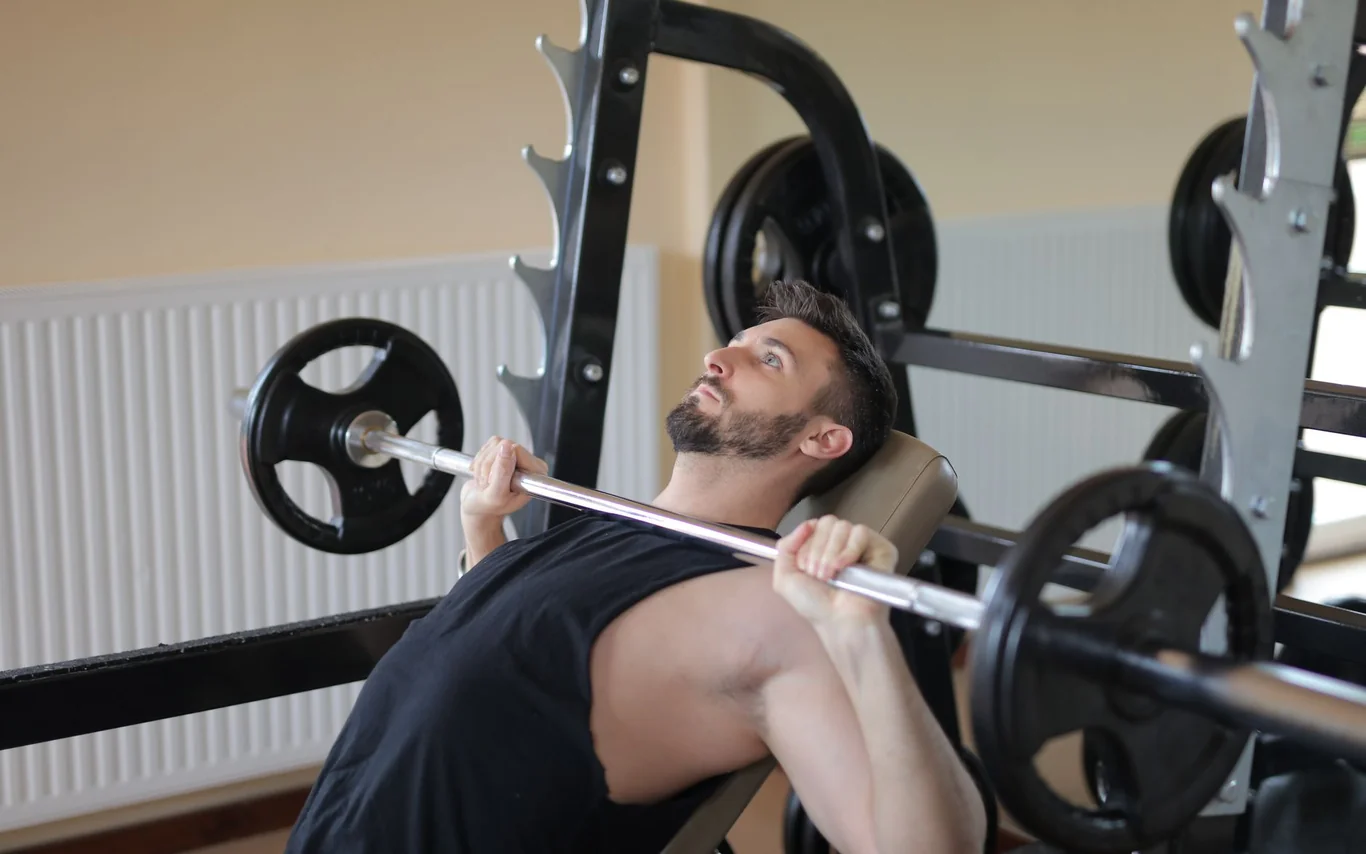 Man performing a barbell bench press on a rack in a gym, focusing on heavy compound lifting