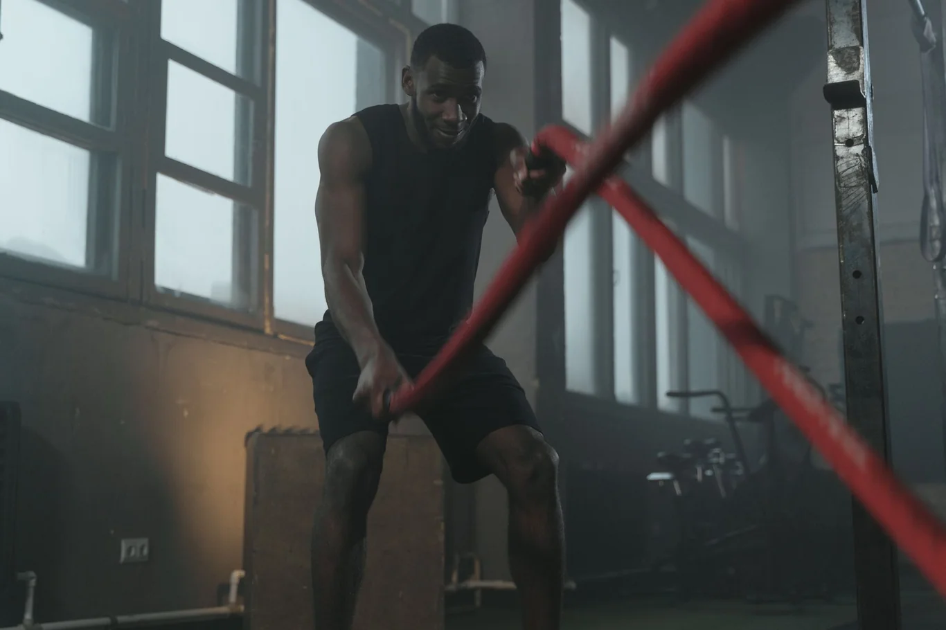 Muscular man gripping battle ropes mid-exercise in a dimly lit gym