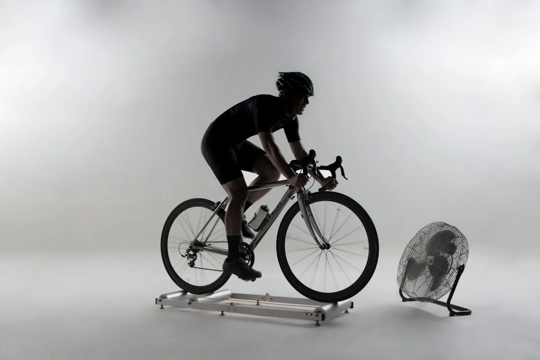 Cyclist riding a road bike on an indoor roller trainer next to a floor fan