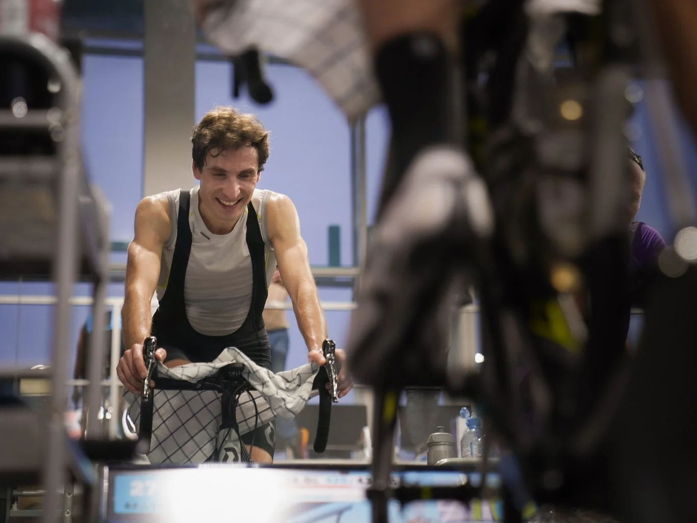 Man smiling while riding an indoor cycling bike during a spin class with other cyclists in the background