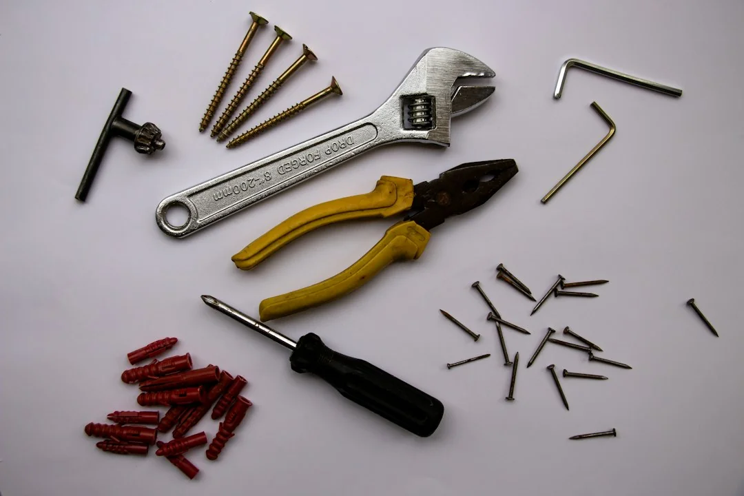 Wrench, pliers, screwdriver, hex key, screws, and wall anchors laid out on a white surface
