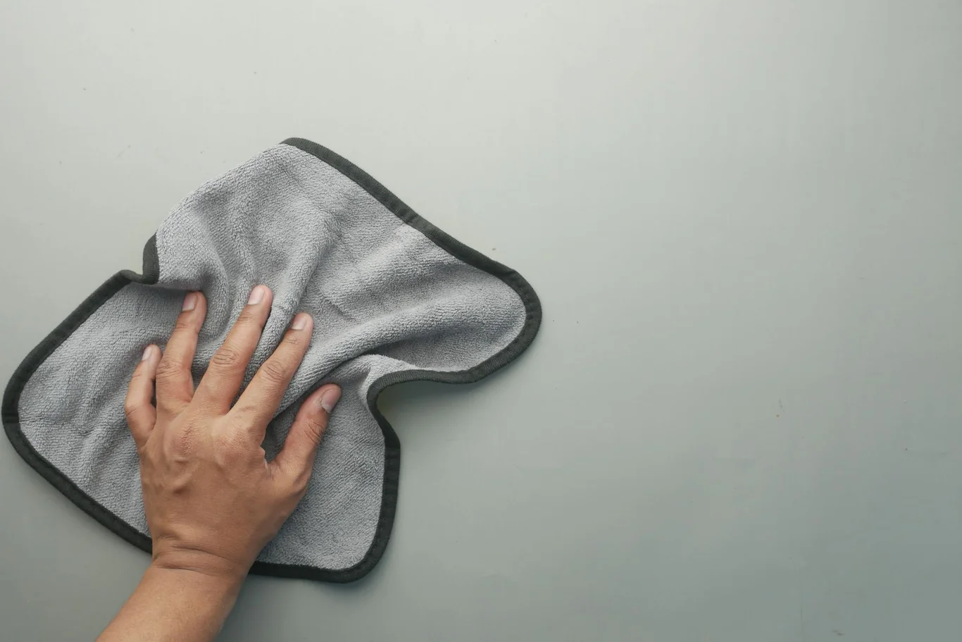 Hand wiping a flat surface with a soft gray microfiber cloth