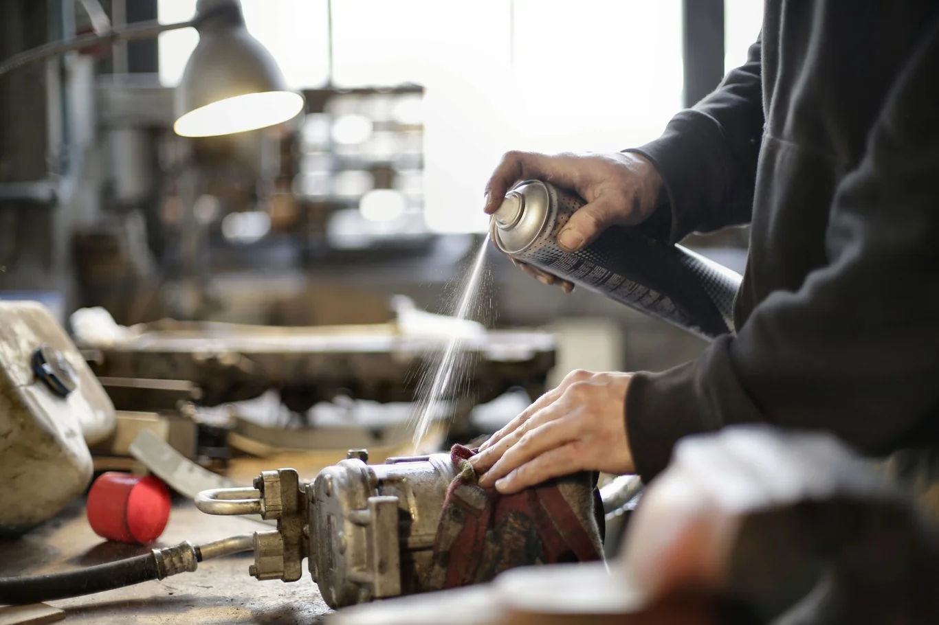 Person applying spray lubricant to a mechanical part in a workshop