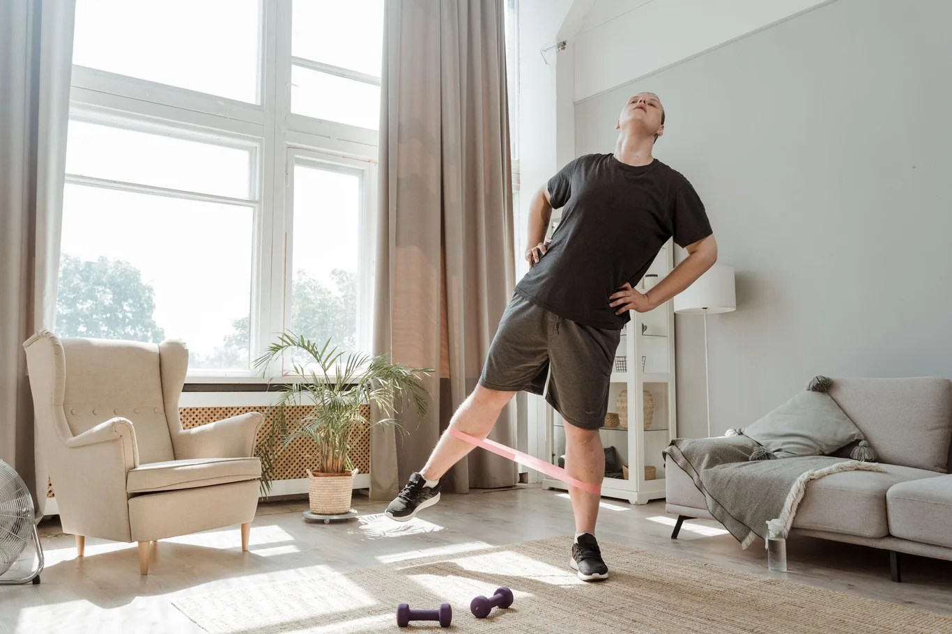 Man performing resistance band leg exercises in a sunlit living room