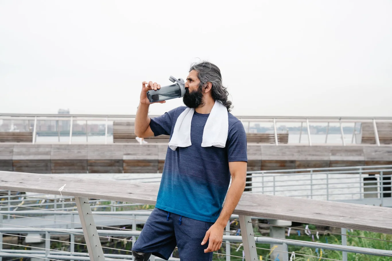 Man in athletic wear drinking from a water bottle on an outdoor waterfront path