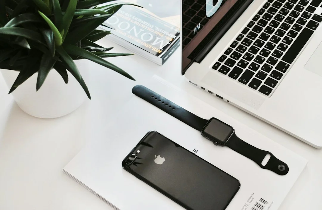 Apple Watch and iPhone on a white desk beside a MacBook keyboard and small potted plant