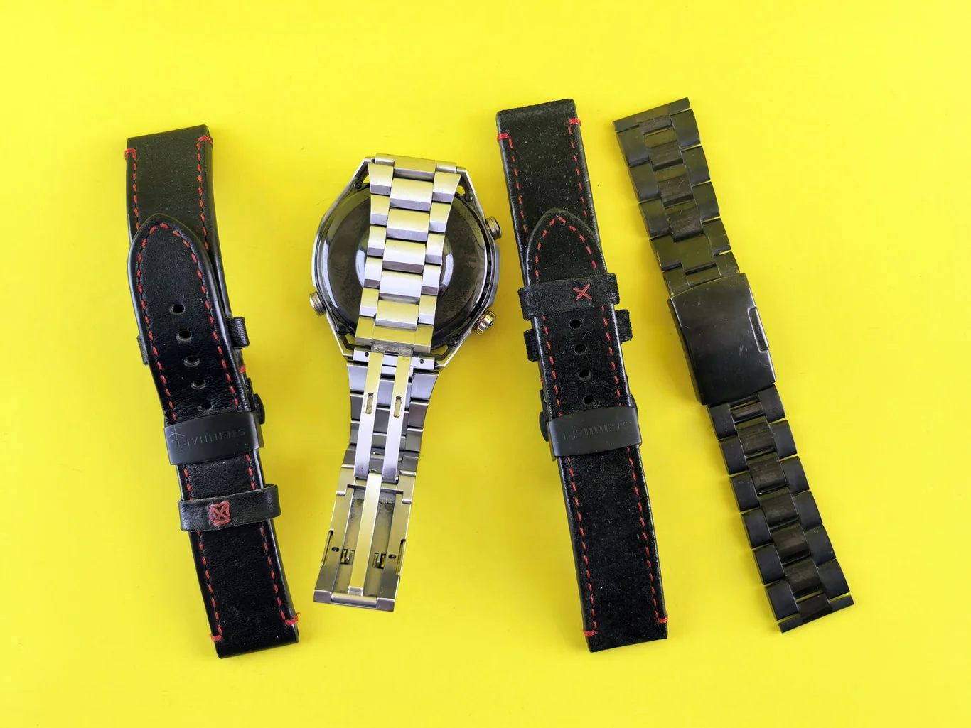 Smartwatch with four replacement bands including leather and metal options laid flat on yellow surface