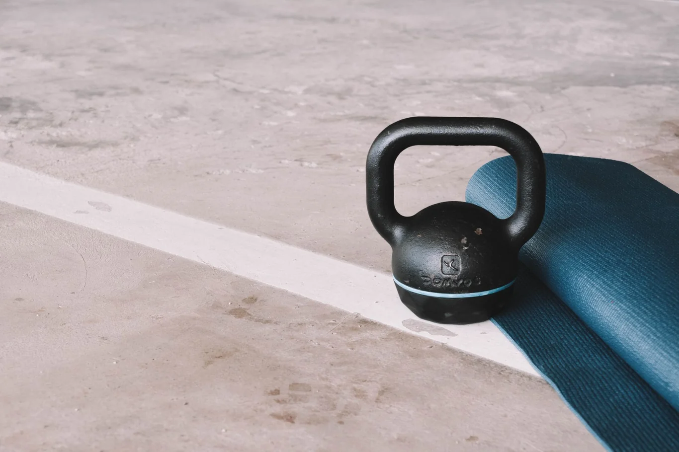Black kettlebell resting on a blue yoga mat on a concrete floor in natural light