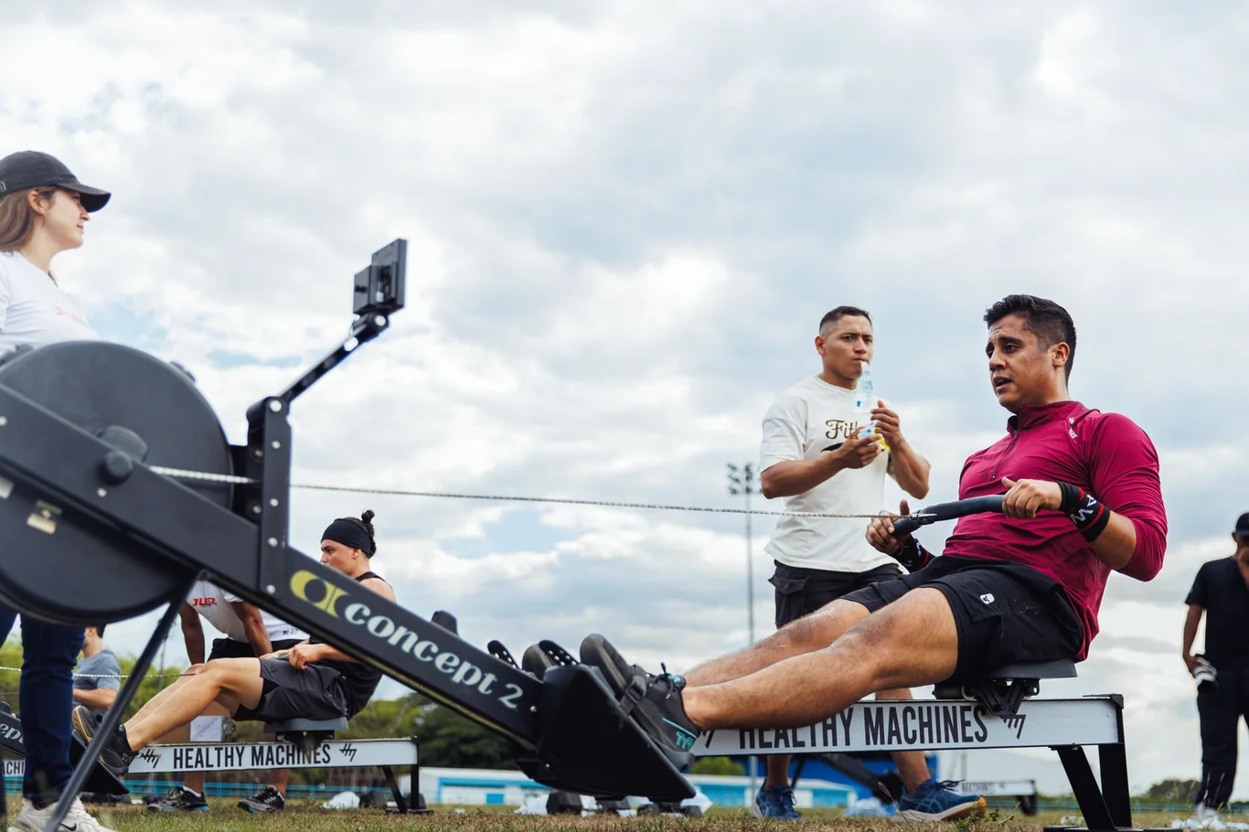 Man in red shirt rowing on a Concept2 rowing machine at an outdoor fitness event