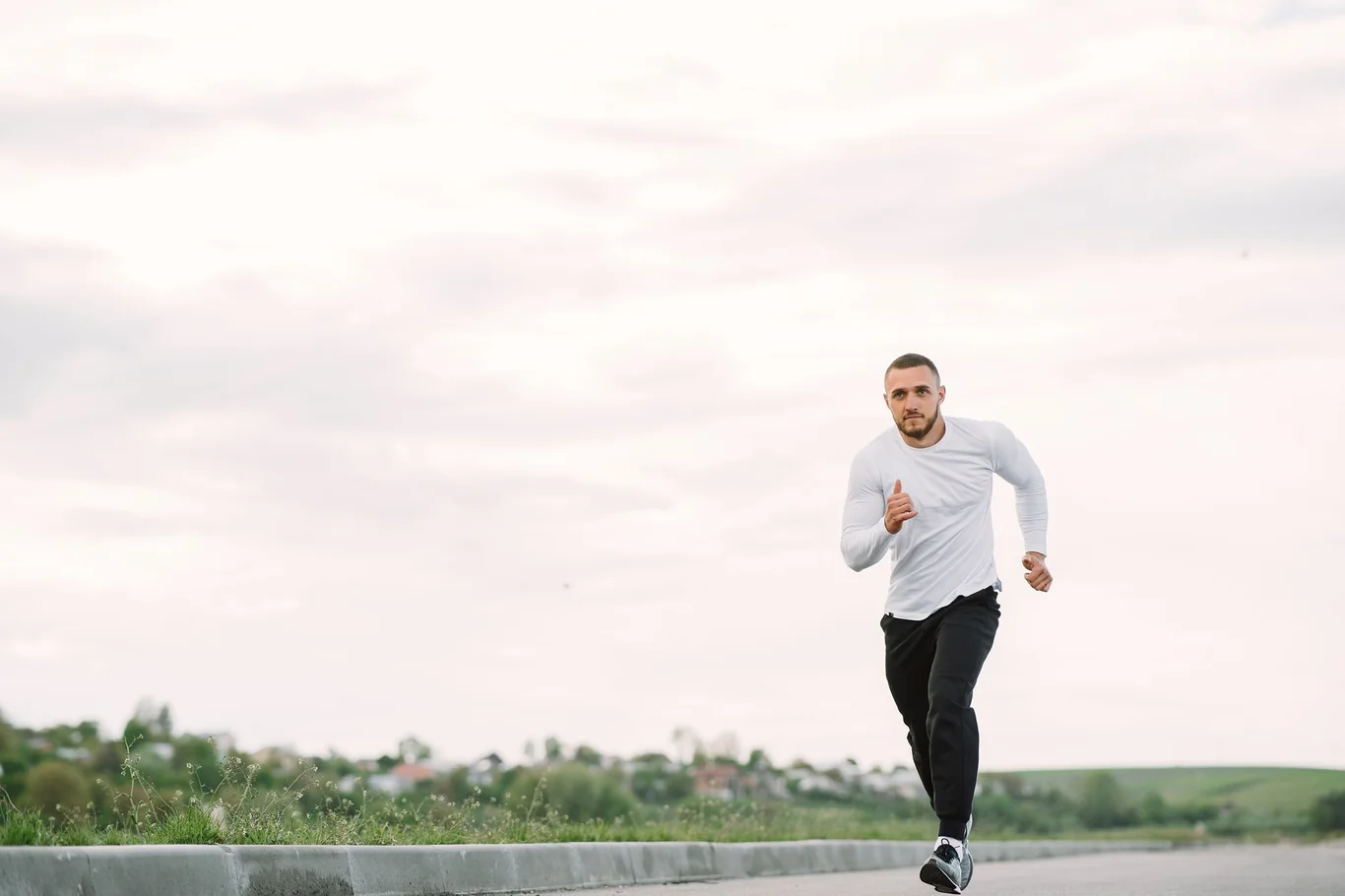 Man in a white long-sleeve shirt running on an open road under a cloudy morning sky