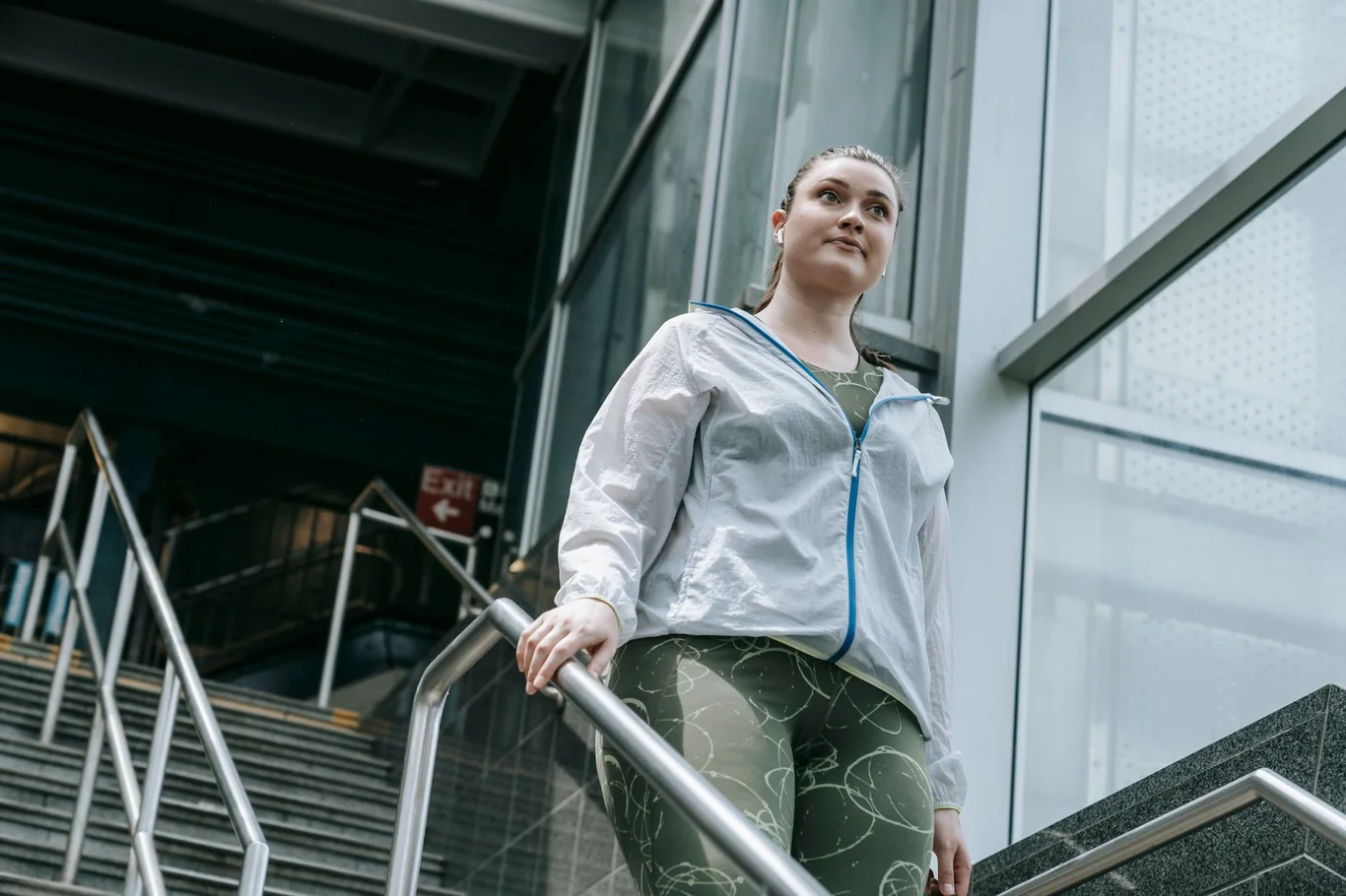Woman in athletic wear walking up outdoor stairs while holding the railing