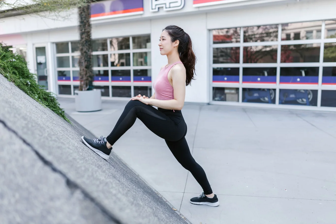 Woman in athletic wear performing a lunge stretch on outdoor steps near a gym