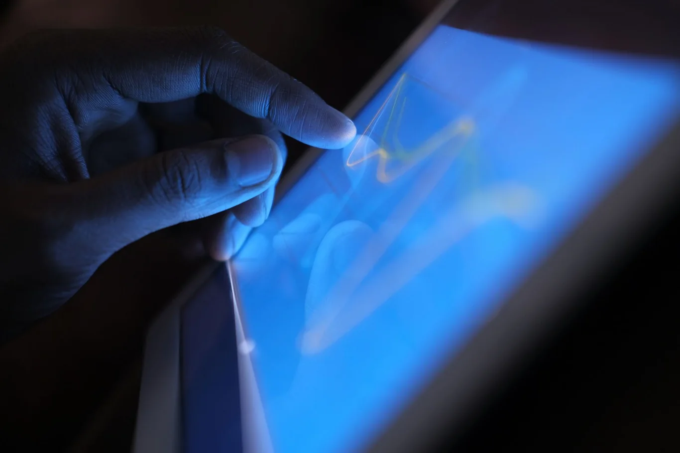 Person's finger tapping a blue-lit tablet screen showing a workout graph in a dark setting