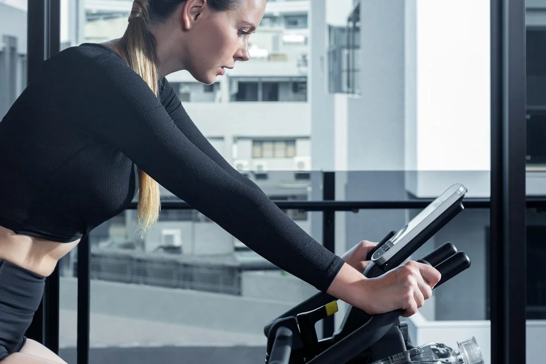 Woman in black athletic wear riding a stationary bike with a tablet screen mounted on the handlebars