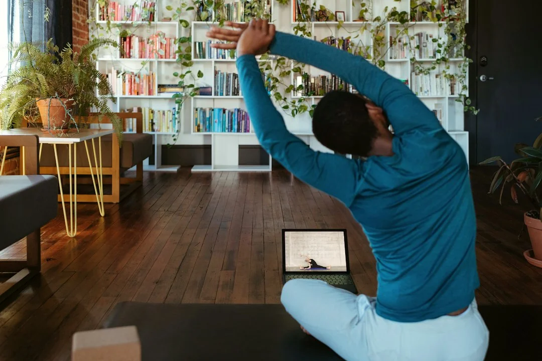 Person stretching at home following a fitness class on a laptop in a plant-filled living room