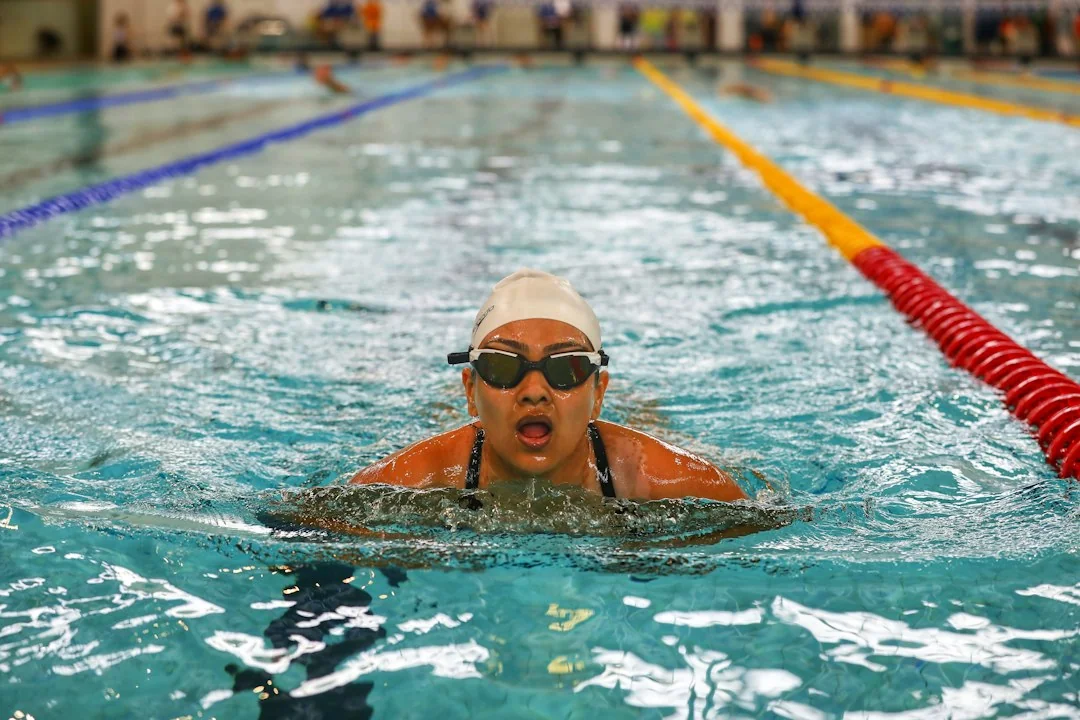 Woman in swim cap and goggles swimming breaststroke in an indoor lap pool