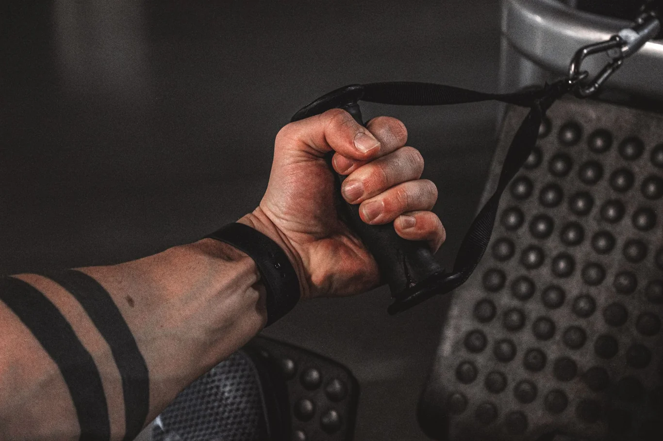 Hand gripping a rowing machine strap handle with a chain and textured foot plate in the background