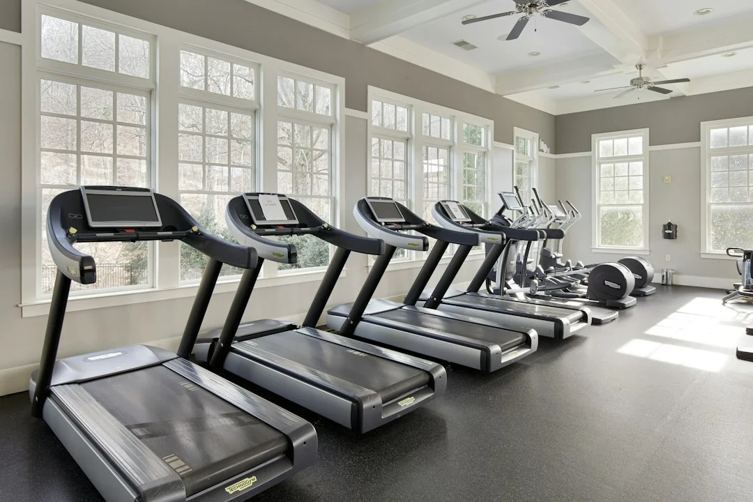 Row of treadmills in a bright, modern home gym with large windows and a ceiling fan