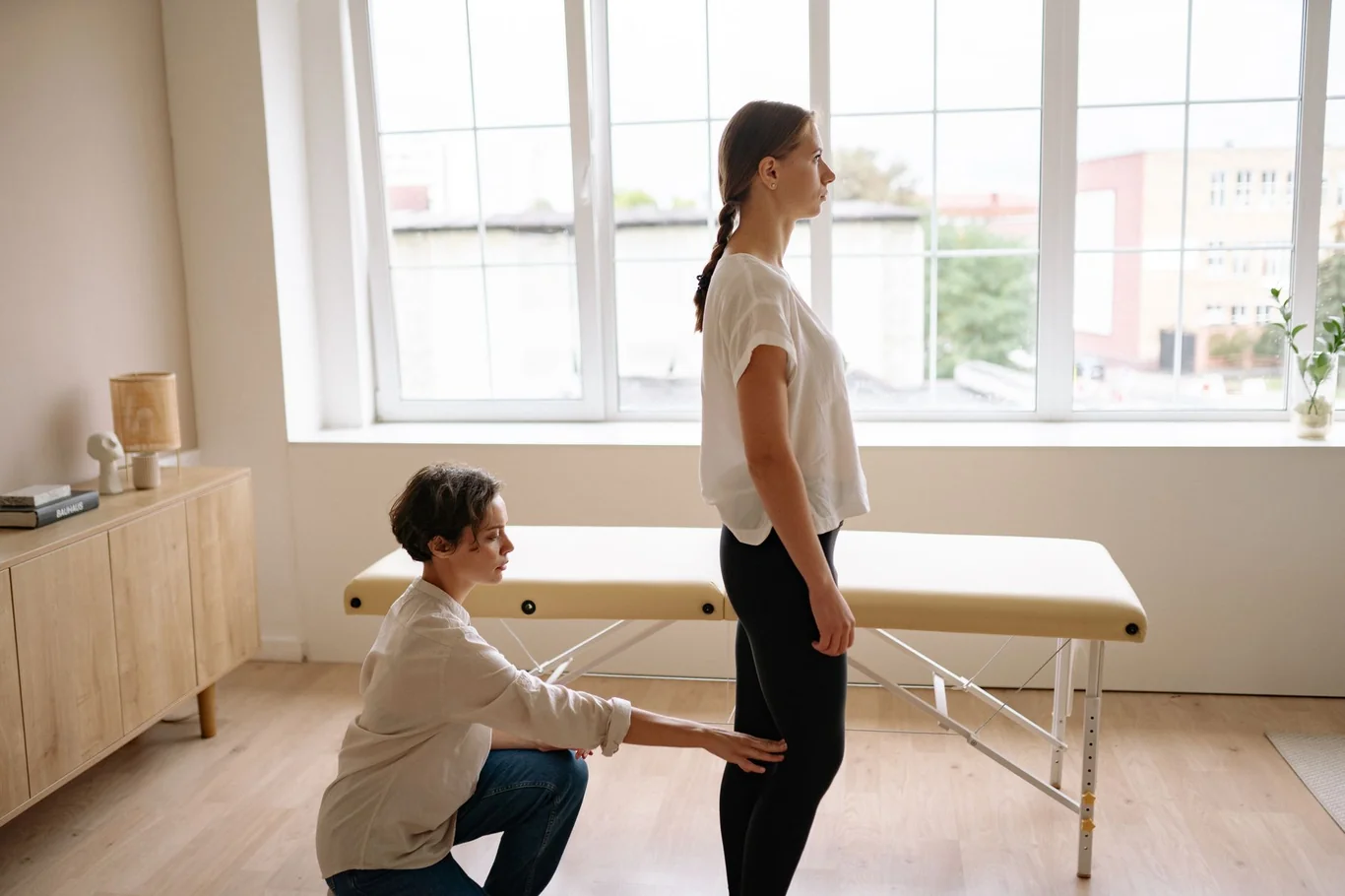 Trainer checking a woman's standing posture and alignment in a bright studio