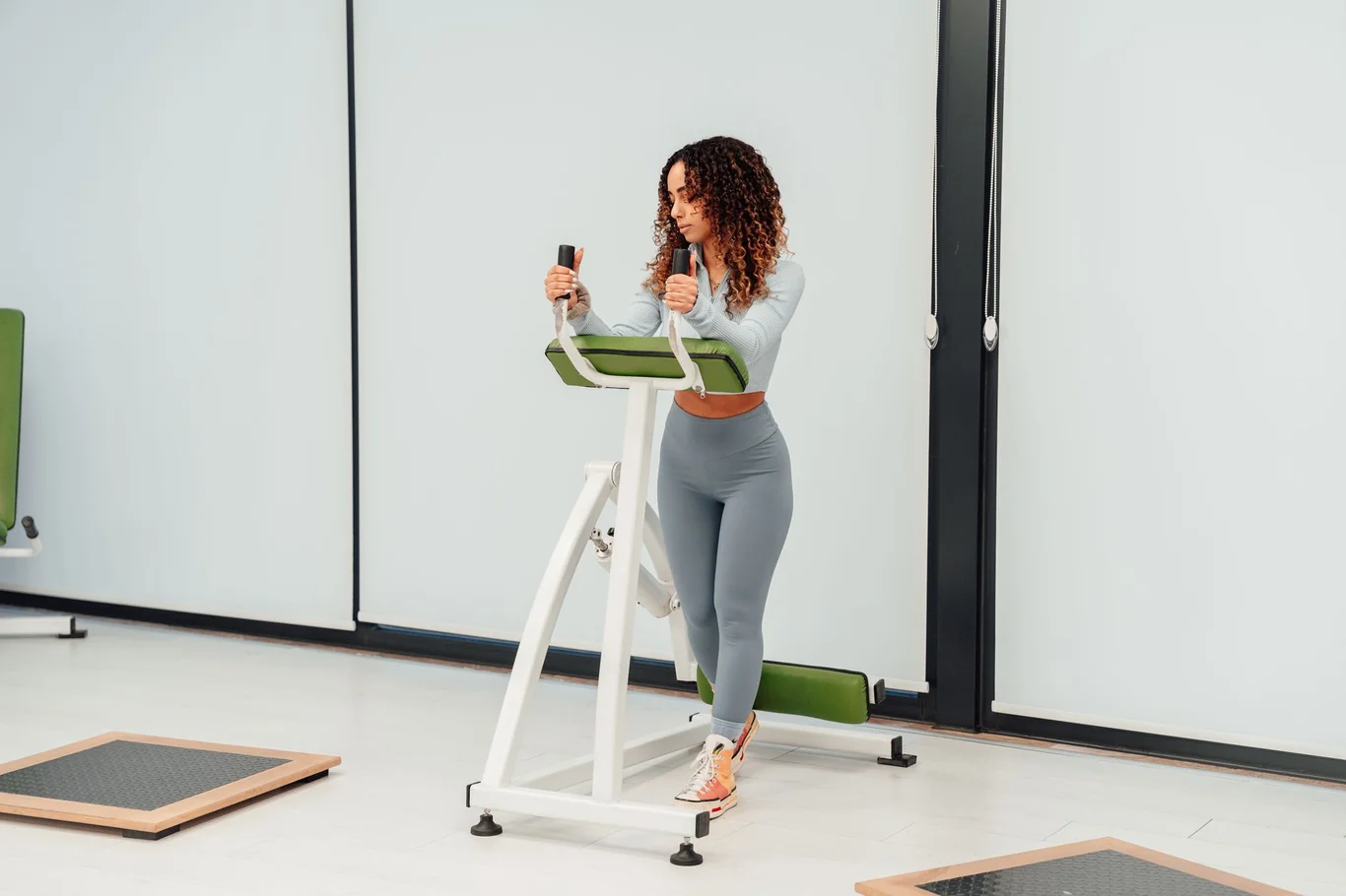 Woman with curly hair stepping on a mini stepper machine in a bright gym